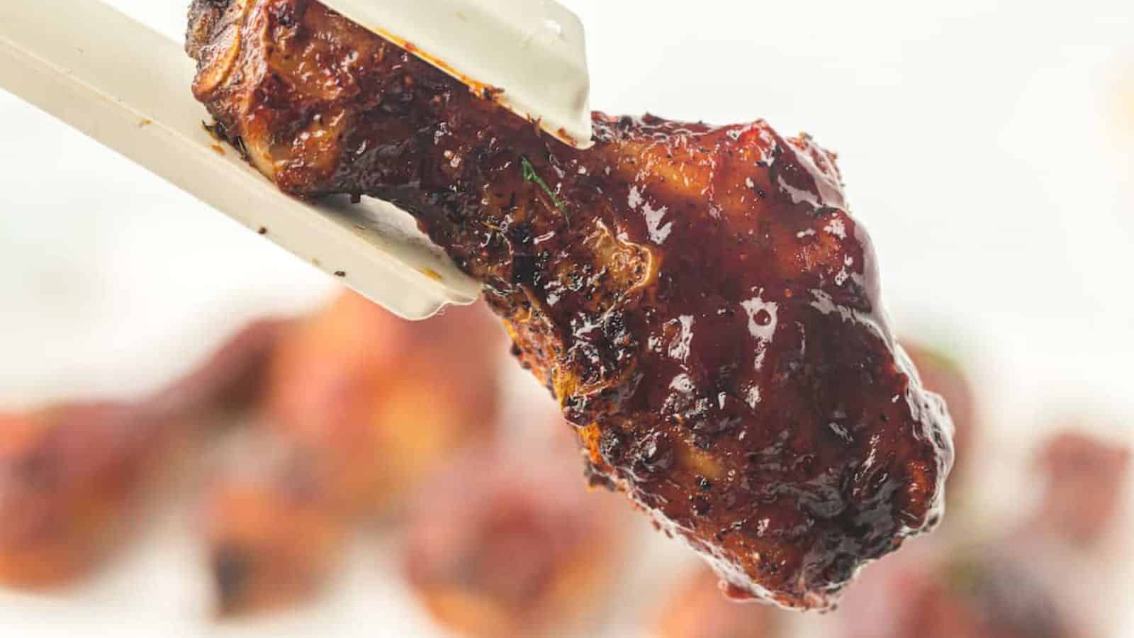 A close-up of chopsticks holding a piece of glazed, grilled chicken. The chicken appears juicy and well-cooked.