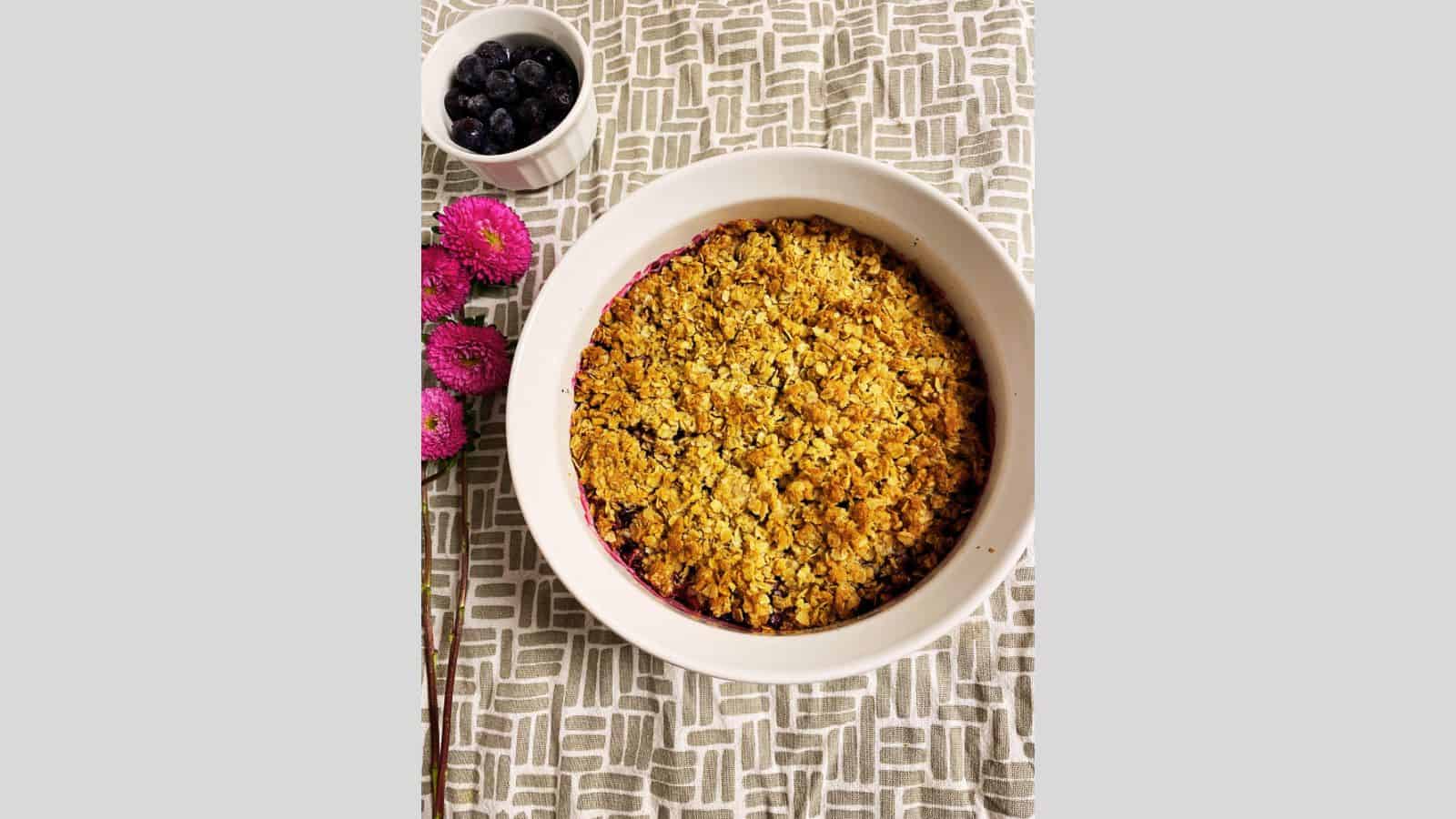 A bowl of berry crumble sitting next to flowers.