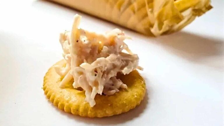 A cracker topped with shredded cheese and what appears to be a creamy chicken mixture. An opened cracker package is visible in the background.