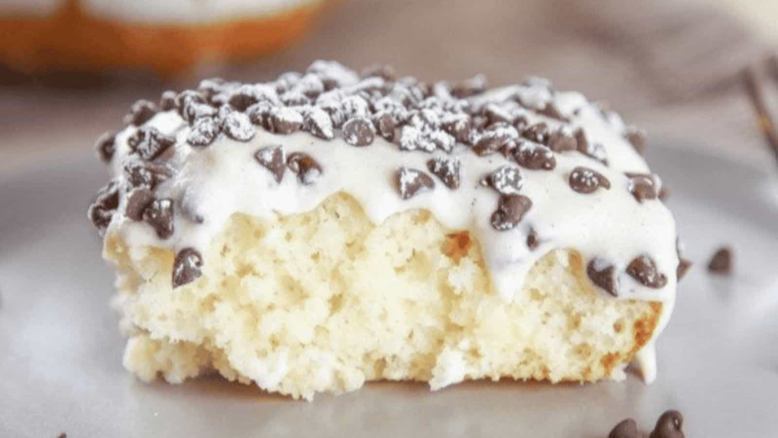 A slice of cannoli cake topped with cannoli cream frosting, mini chocolate chips and powdered sugar.