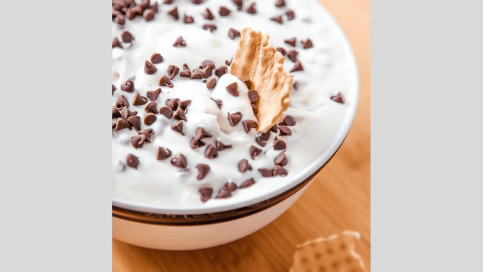 A waffle cone chip dipping into cannoli dip topped with chocolate chips.