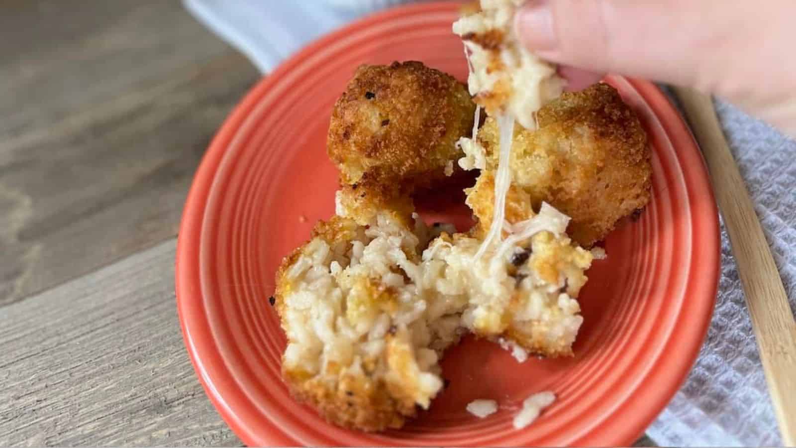 A person pulling apart a gooey, cheese-filled arancini with more of the fried rice balls and sauce in the background.