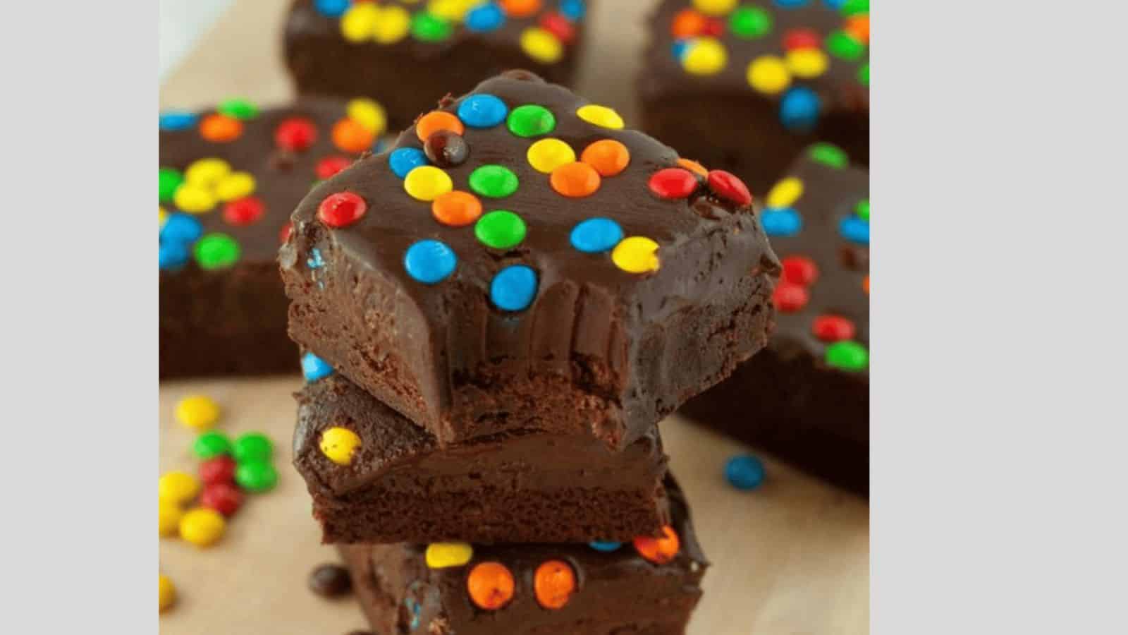 Thick stacked brownies topped with chocolate ganache and mini M&Ms.