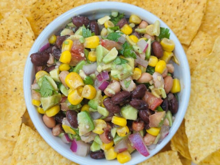 A bowl filled with a colorful mix of corn, black beans, diced avocado, red onion, and chopped herbs, surrounded by tortilla chips.