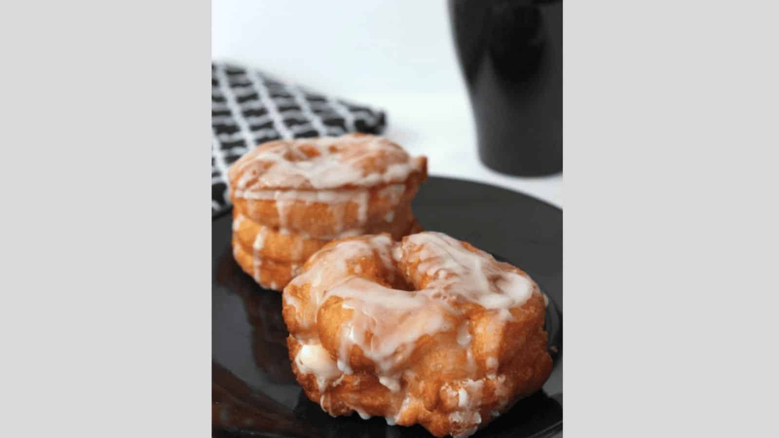 A glazed cronut on a black plate.