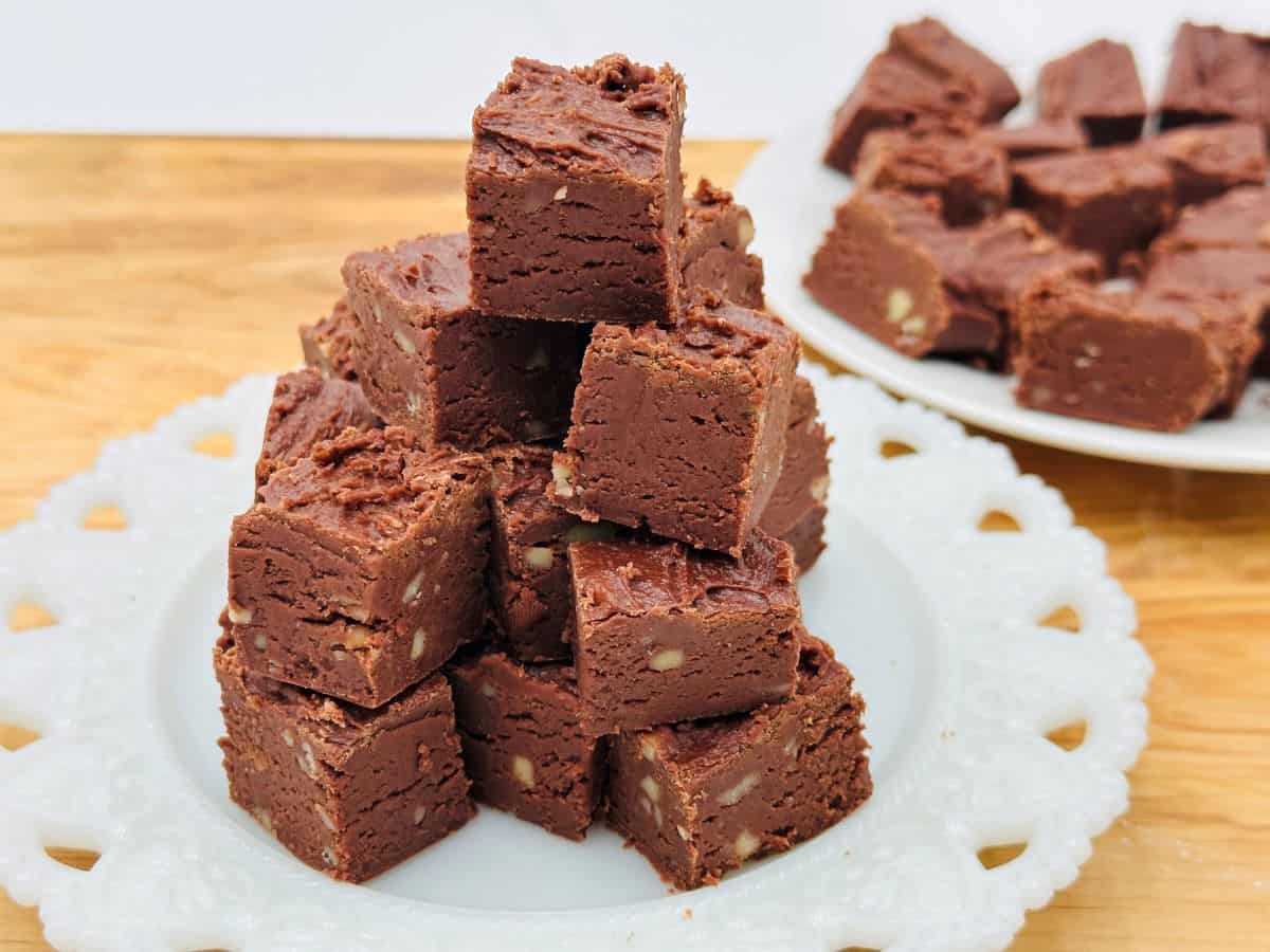 A plate of chocolate fudge squares is stacked into a pyramid, with another plate of fudge squares in the background.