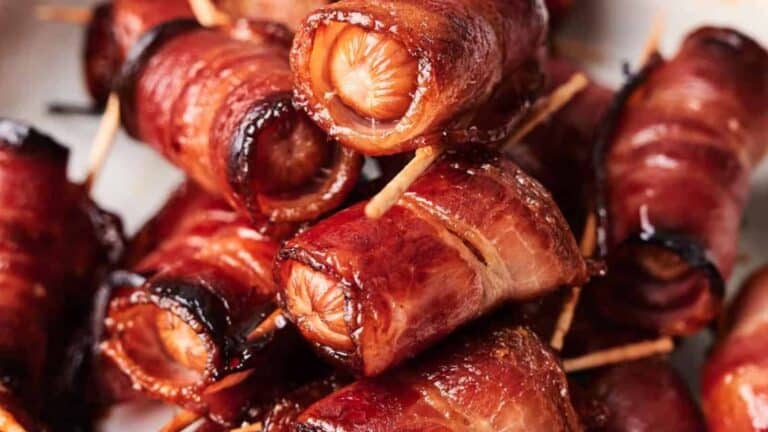 Close-up of cooked bacon-wrapped sausages held together with toothpicks. The sausages are browned and caramelized.