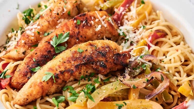 A plate of spaghetti topped with grilled chicken strips, sliced peppers, and garnished with chopped parsley and grated cheese.