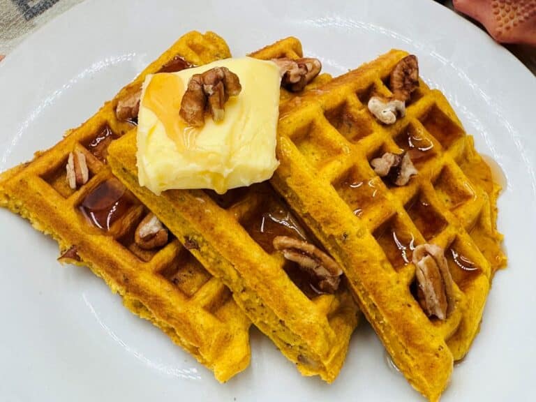 A plate of three pumpkin waffles topped with pecans, a pat of butter, and drizzled with syrup.