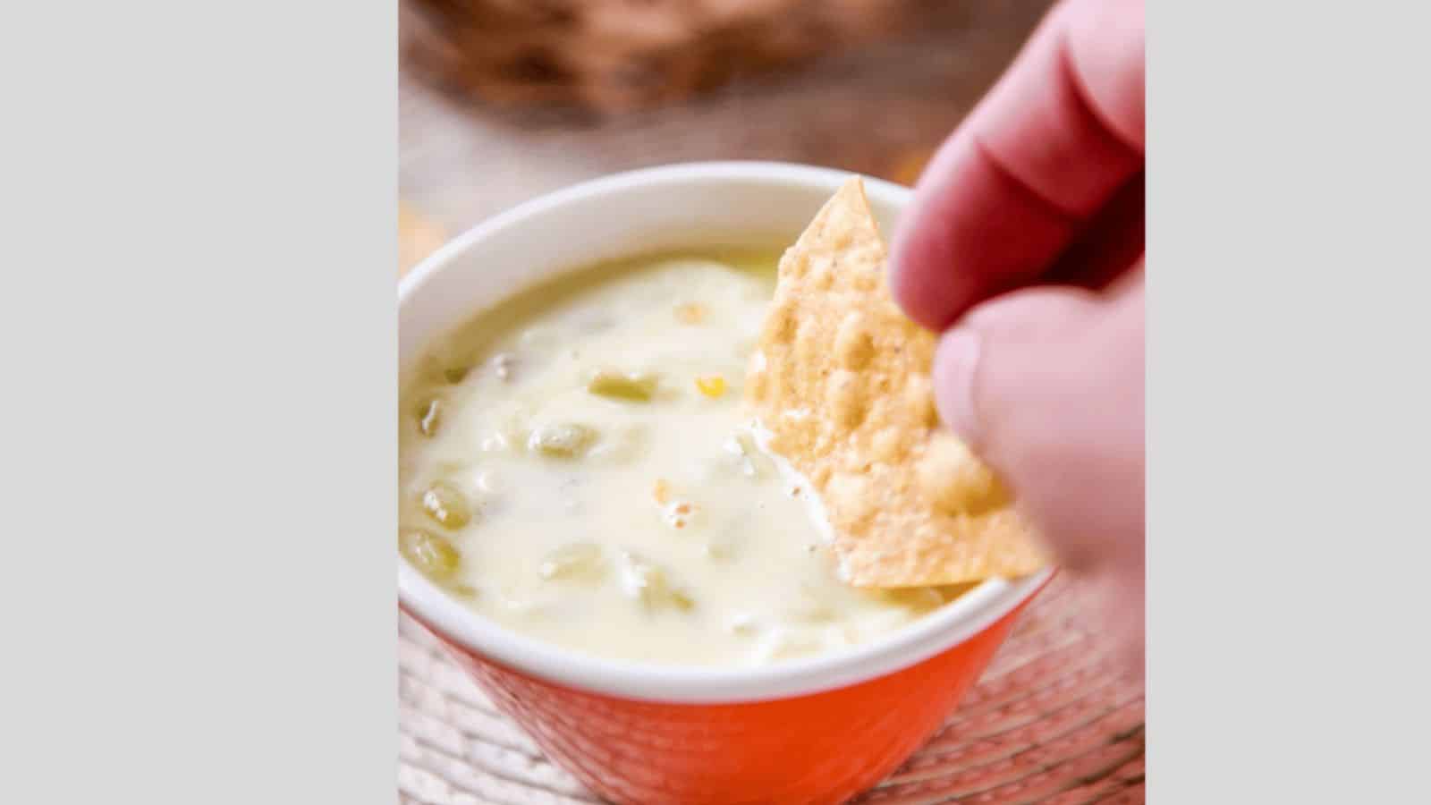 A tortilla dip dipping into white queso sauce with green chiles.