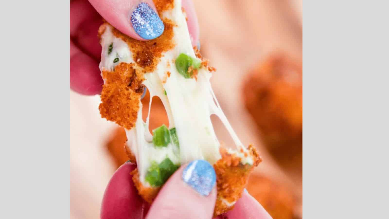 A hand with blue nail polish pulling apart a cheesy rattlesnake bite with jalapenos.