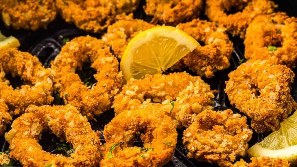 Close-up of crispy, golden-brown fried calamari rings garnished with parsley and lemon slices.