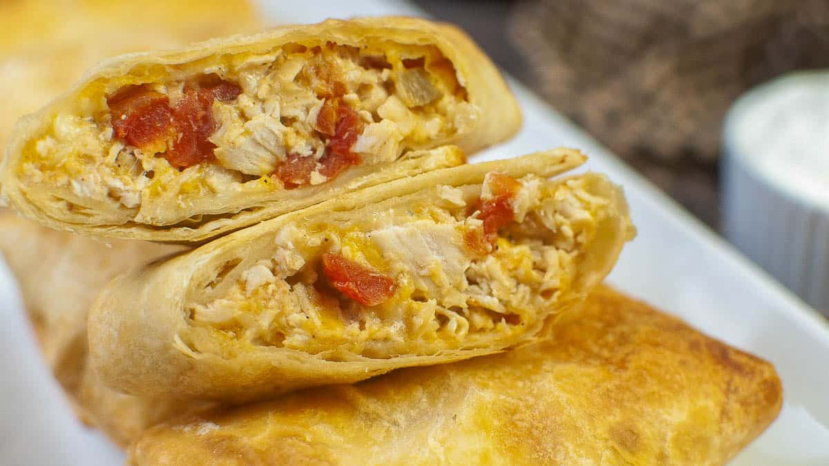 Close-up of a Chimichanga cut in half, showing the filling, served on a white plate.