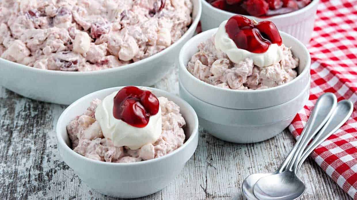 A bowl of cranberry salad with whipped cream and cherries.