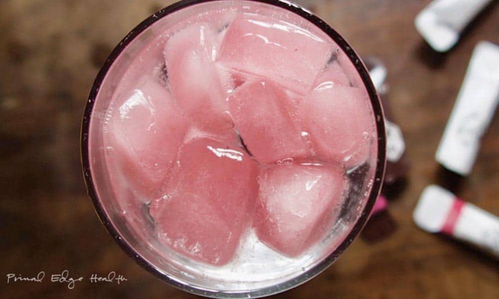 A top view of a glass filled with pink-colored ice cubes and water.