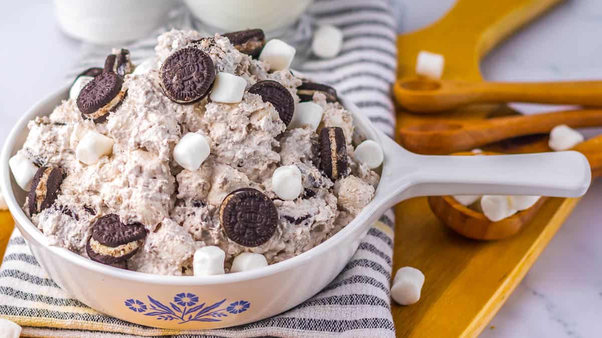 A white dish filled with a creamy dessert mixed with mini chocolate sandwich cookies and small marshmallows.