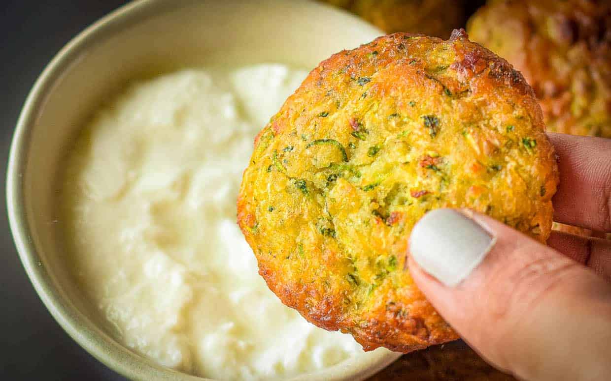 Zucchini fritter getting dipped into sauce.