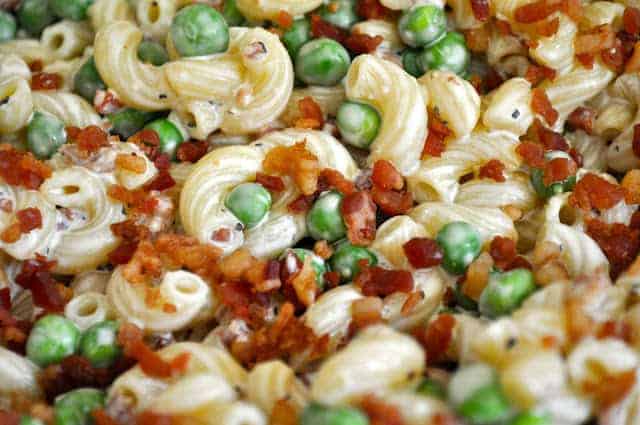 Close-up of a macaroni salad with peas and bacon bits mixed with a creamy dressing.