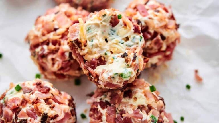 Close-up of several bacon-wrapped cheese balls garnished with chopped herbs on a white surface.