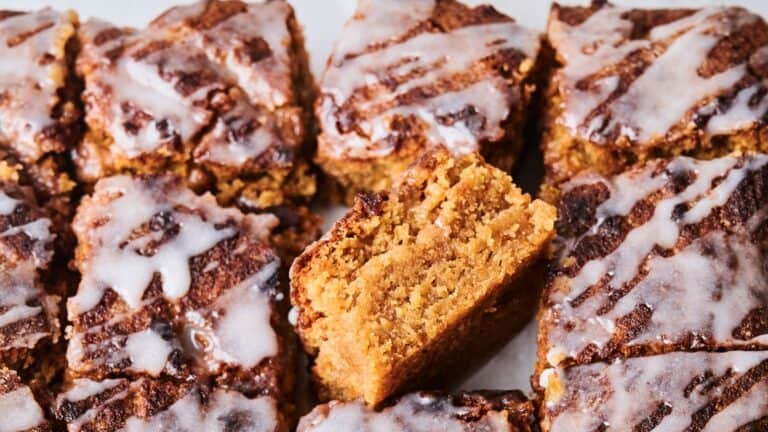 Close-up of sliced pumpkin cake squares topped with white icing, highlighting the warm, moist texture of one piece turned upright.