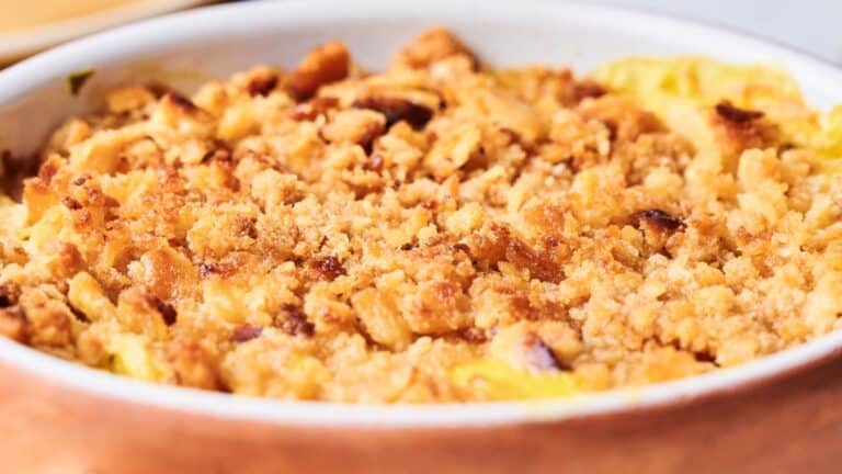 A close-up of a baked dish with a golden, crumbly topping in a round, white ceramic dish.