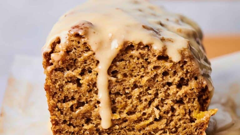 Close-up of a partially sliced loaf of bread with a light glaze drizzled over the top, revealing the moist and textured interior.