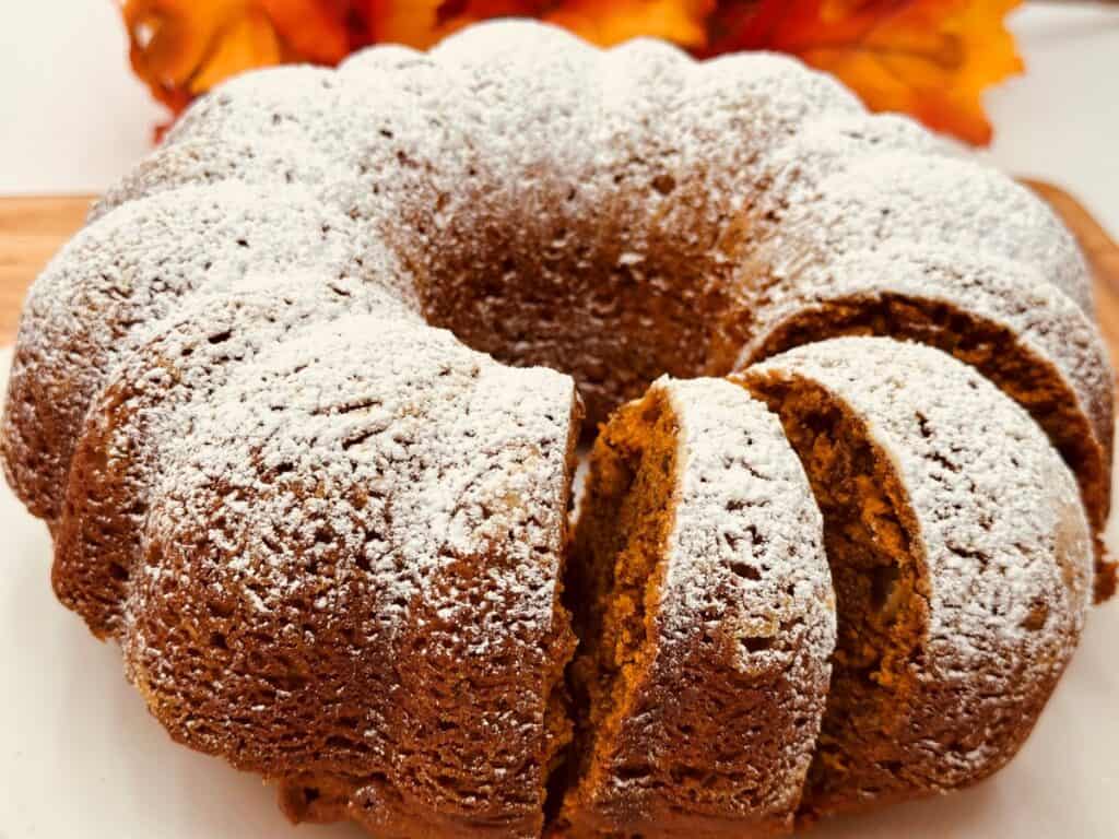 A round bundt cake topped with powdered sugar, with a few slices cut from it.