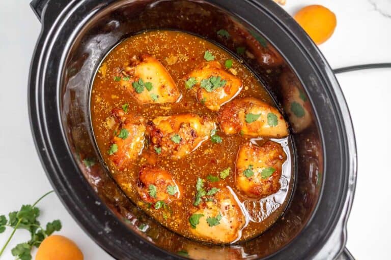 A slow cooker filled with pieces of cooked chicken in a rich, orange-colored sauce, garnished with chopped cilantro.