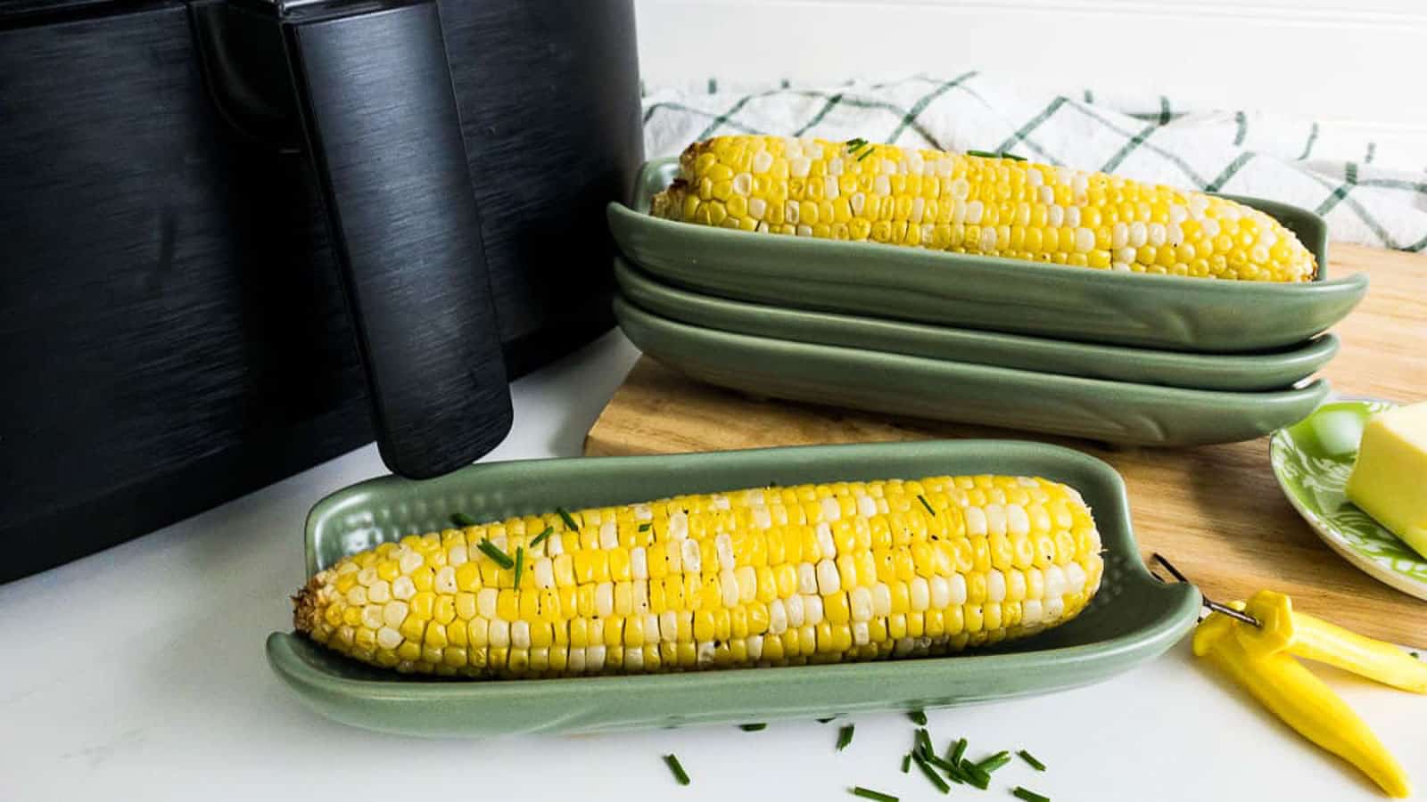 Corn on the cob in a green corn dish in front of an air fryer.