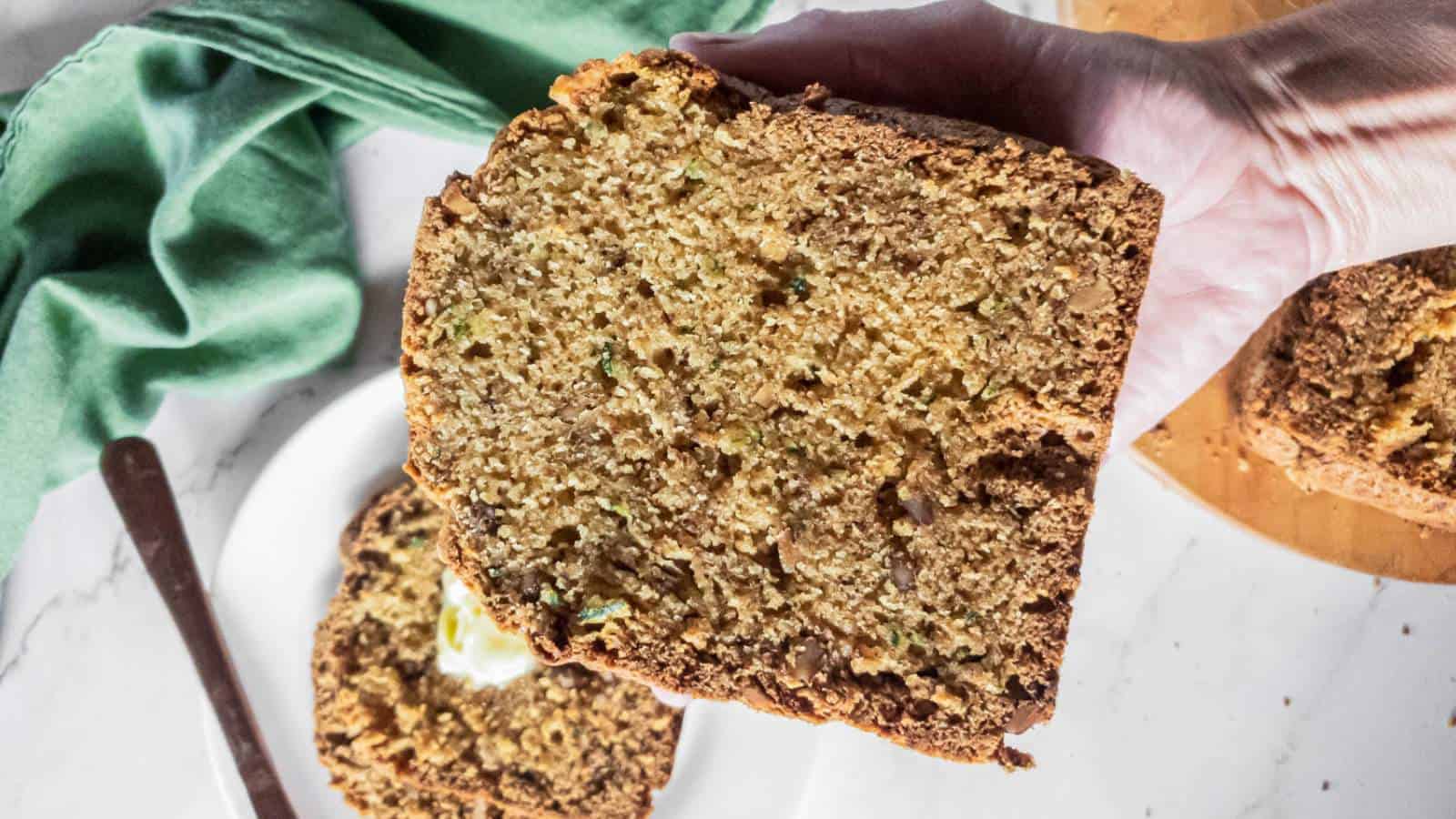 A hand holds a slice of bread machine zucchini bread.