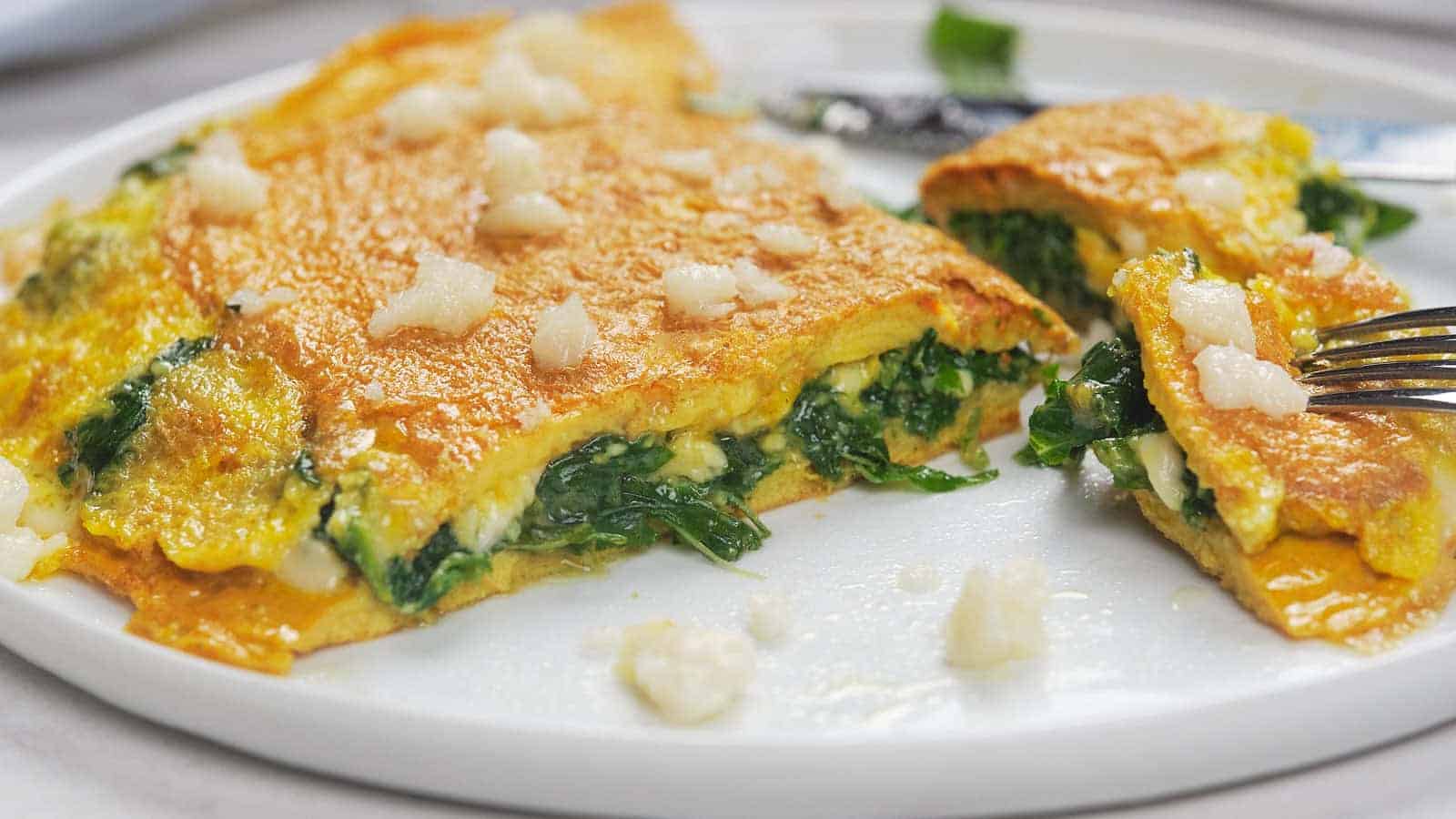 A spinach and cheese omelette on a white plate, cut into pieces, with a few bites taken.