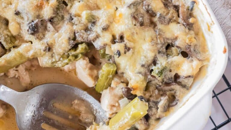 A close-up of a baked casserole with melted cheese, mushrooms, asparagus, and pieces of chicken.