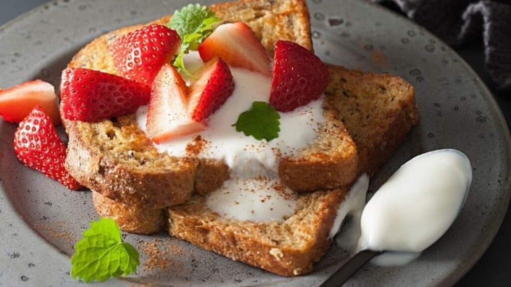 Two slices of toasted bread topped with yogurt, sliced strawberries, and mint leaves.