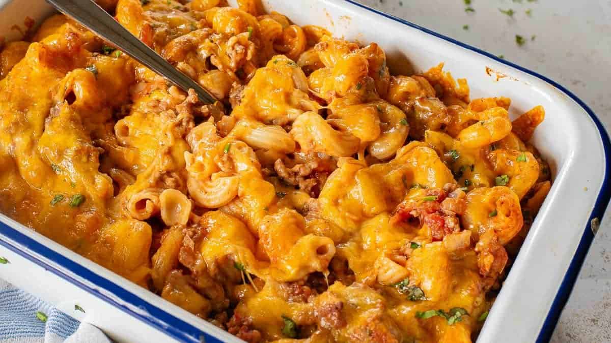 A baking dish filled with baked pasta covered in melted cheese and garnished with chopped herbs.