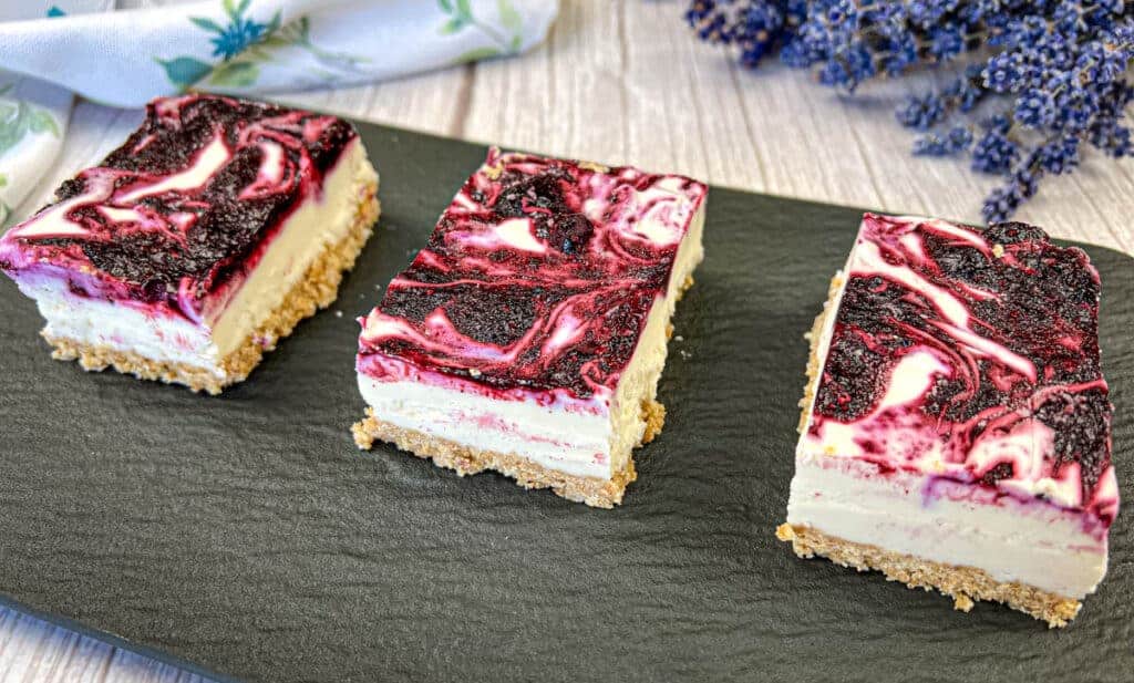 Three slices of Blueberry Cheesecake Bars on a rectangular black slate.