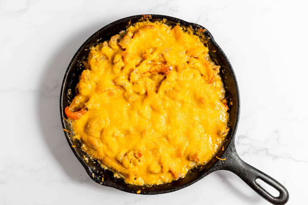 A cast iron skillet filled with baked macaroni and cheese, topped with melted cheddar cheese, on a light marble surface.