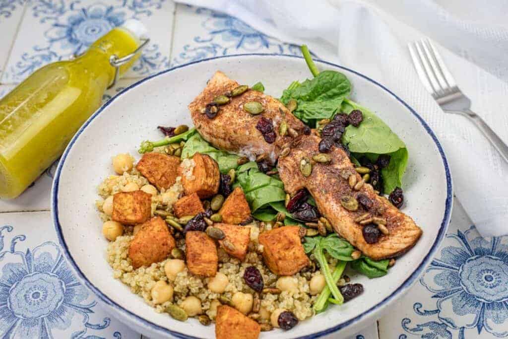 A bowl of Fall Harvest Salmon Bowl with a bottle of dressing and a fork in the background.