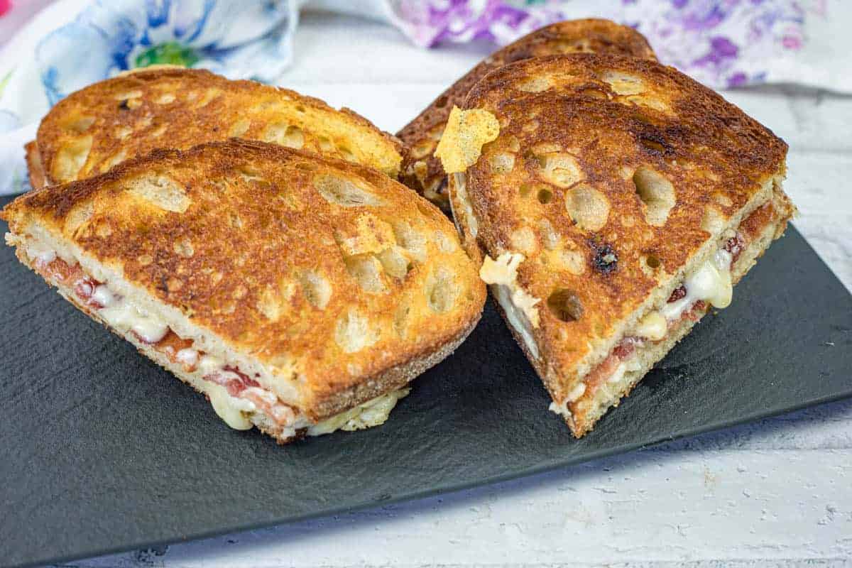 Four grilled cheese sandwiches with hot honey butter on a black slate serving board.