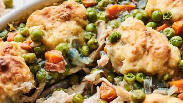 A close-up of a chicken pot pie, featuring chunks of chicken, carrots, peas, and onions, topped with golden-brown biscuits.