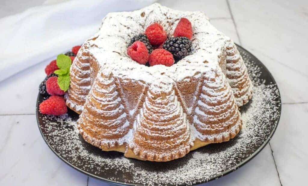 Old Fashioned Whipped Cream Cake dusted with powdered sugar topped with raspberries and blackberries on a black plate.