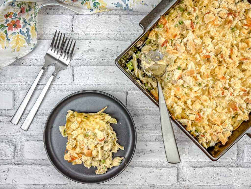 Top-down shot of Tuna Noodle Casserole on a dish with a small portion on a black plate.