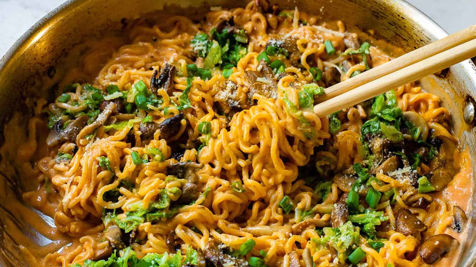 A pan of ramen noodles with mushrooms, greens, and a creamy sauce, served with chopsticks.