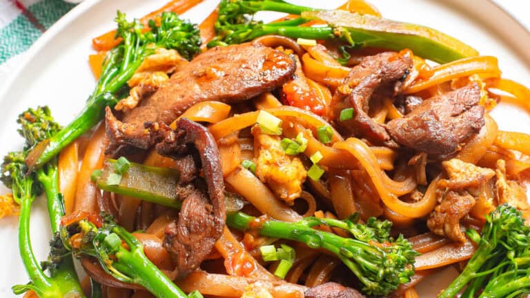 A plate of stir-fried noodles with beef, broccolini, and scrambled eggs.